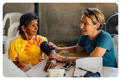 Person checking an elderly woman's blood pressure in a clinical setting.