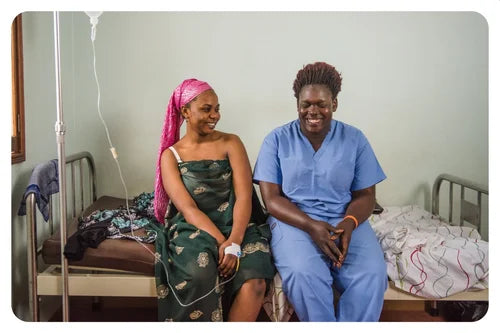 Two women sitting on a bed in a hospital room.